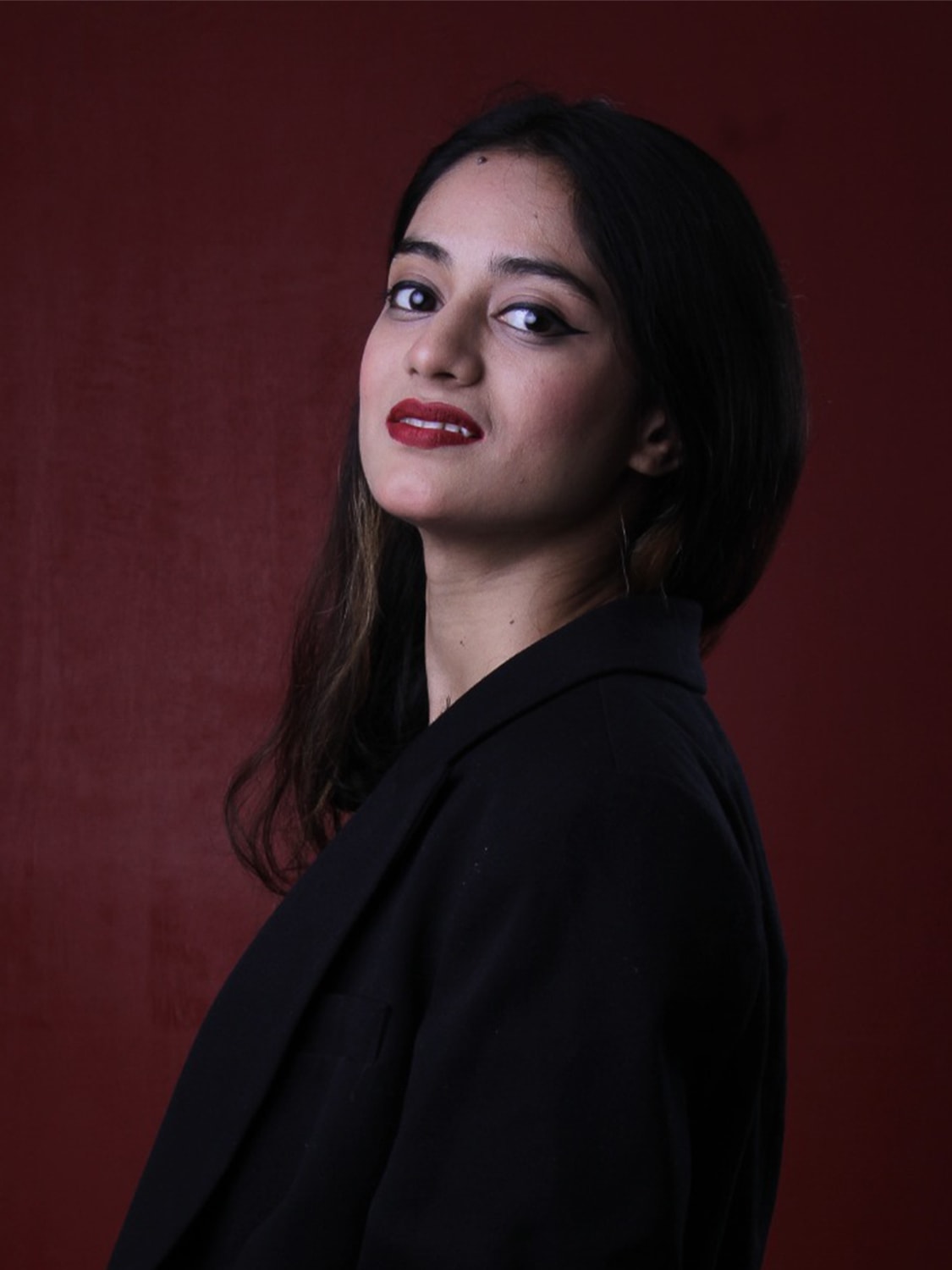 Portrait of Rokaiya Ahmed Purna against a deep red background.