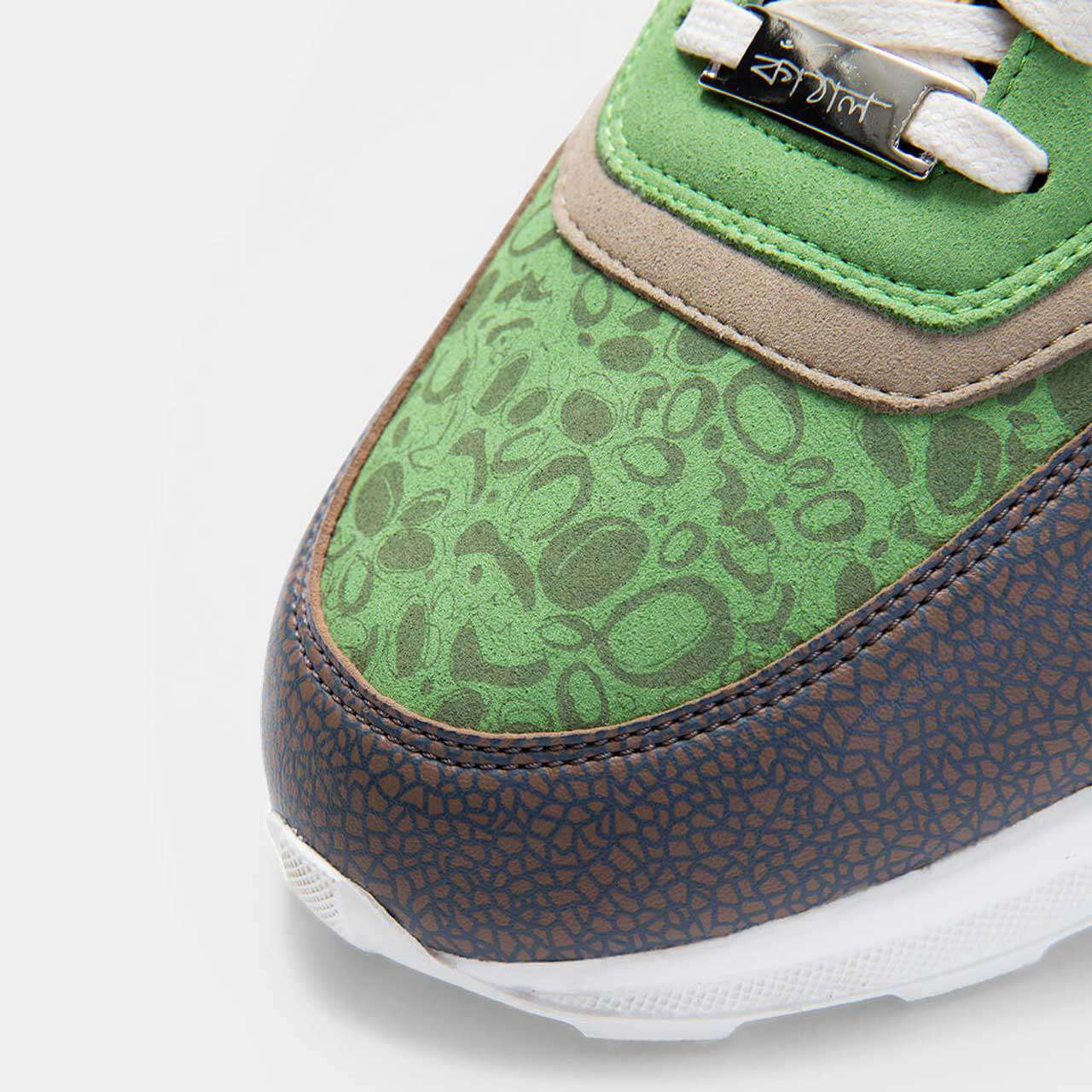 Close-up of a Kamthala sneaker toe with green jackfruit print and a metal lace plaque in Bengali.